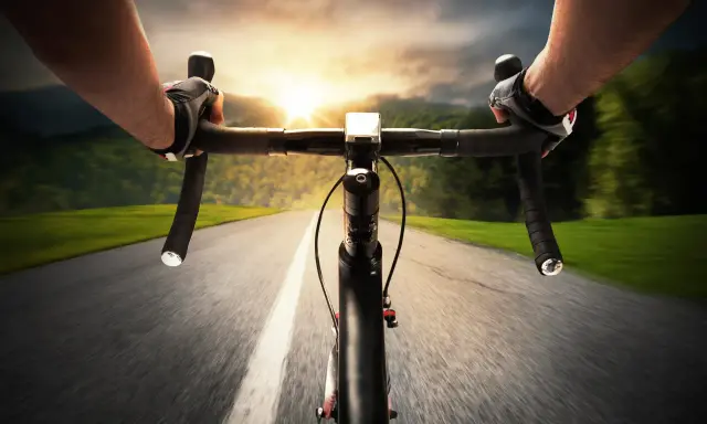 Rowerzysta w rękawiczkach mija pola i lasy, celując w zachód słońca. Dziś na liczniku pojawi się 100 km na rowerze.