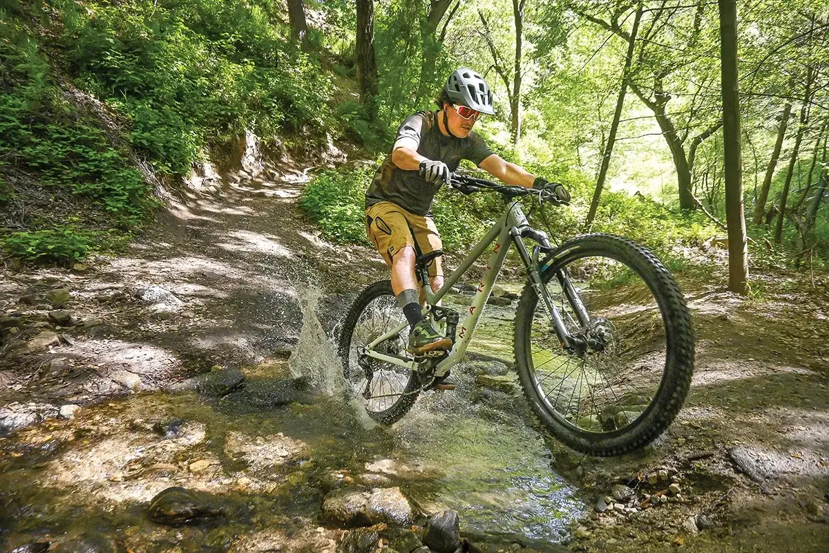 Rowerzysta pokonuje strumień na leśnym szlaku, rozpryskując wodę. To przygoda w marin rift zone.