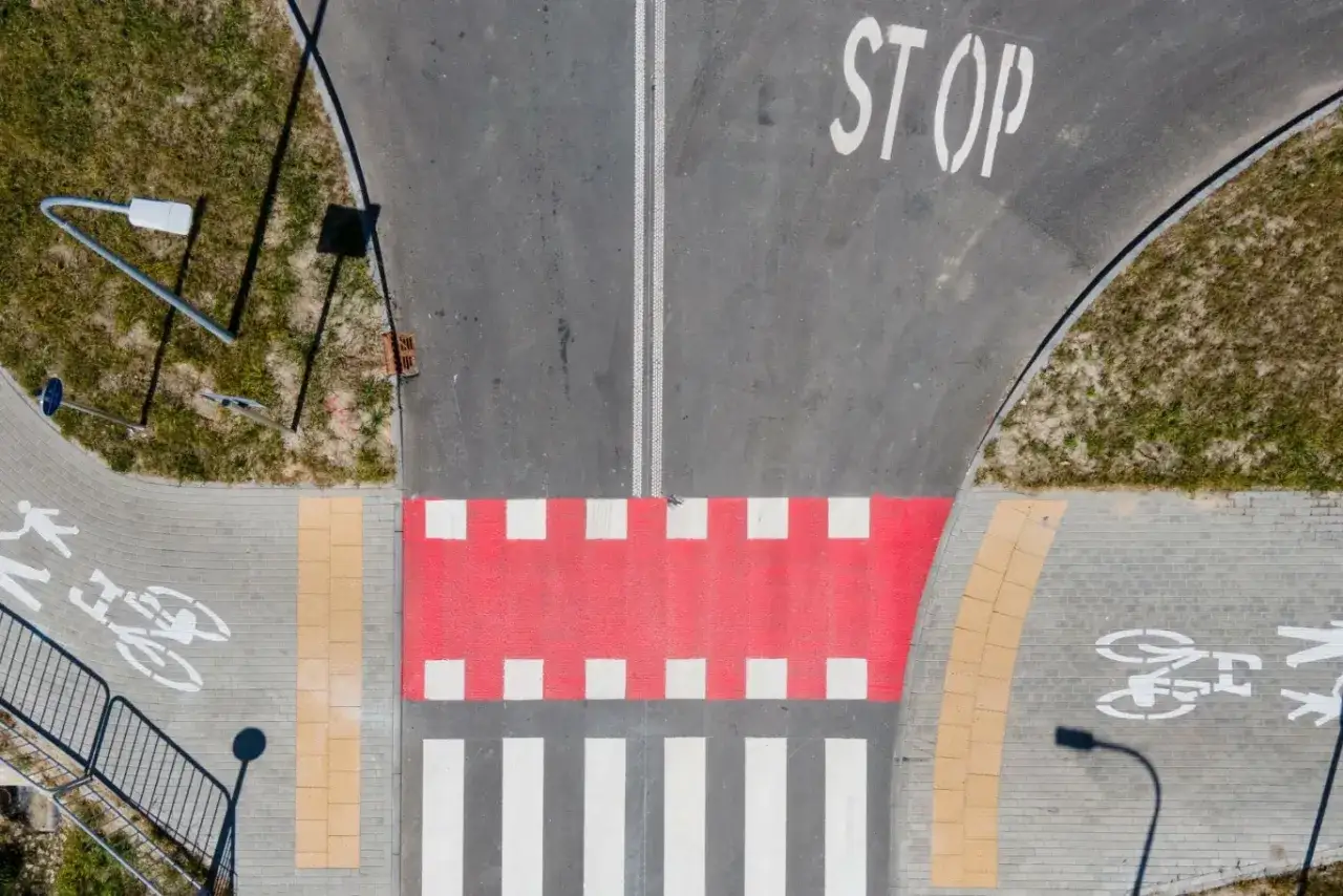 Czerwone pasy dla rowerzystów i pieszych na skrzyżowaniu. Znak STOP na drodze.