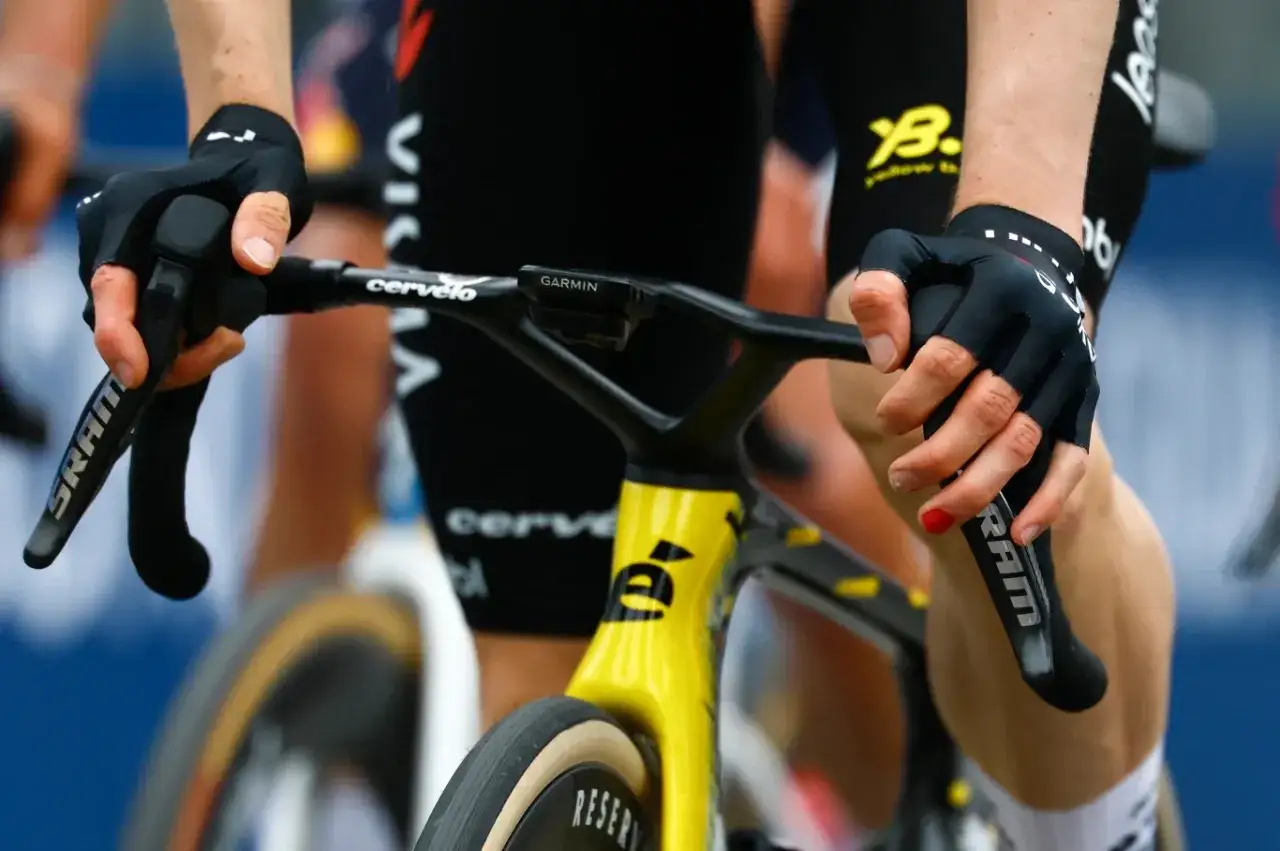 Ręce w rękawiczkach na kierownicy roweru szosowego. Pokazuje, jak zmieniać przerzutki w rowerze szosowym, naciskając manetki SRAM.