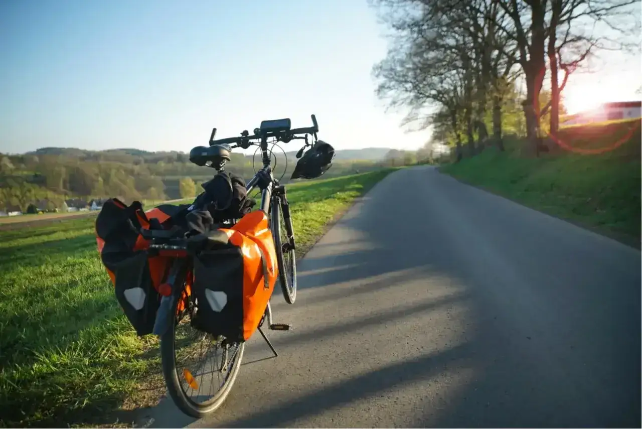 Rower z sakwami gotowy na wyprawę. Ile czasu zajmie przejechanie 100 km rowerem? Słońce zachodzi nad malowniczą drogą.