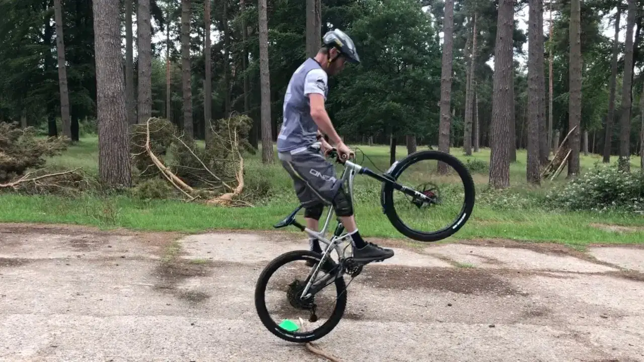 Kolarz w kasku wykonuje bunny hop na rowerze w lesie.