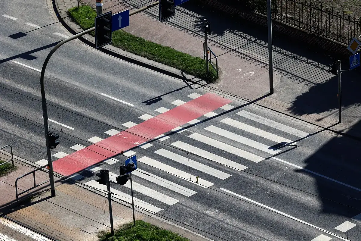 Przejazd dla rowerów z czerwonym pasem i białymi pasami na drodze, sygnalizacja świetlna i znaki drogowe.