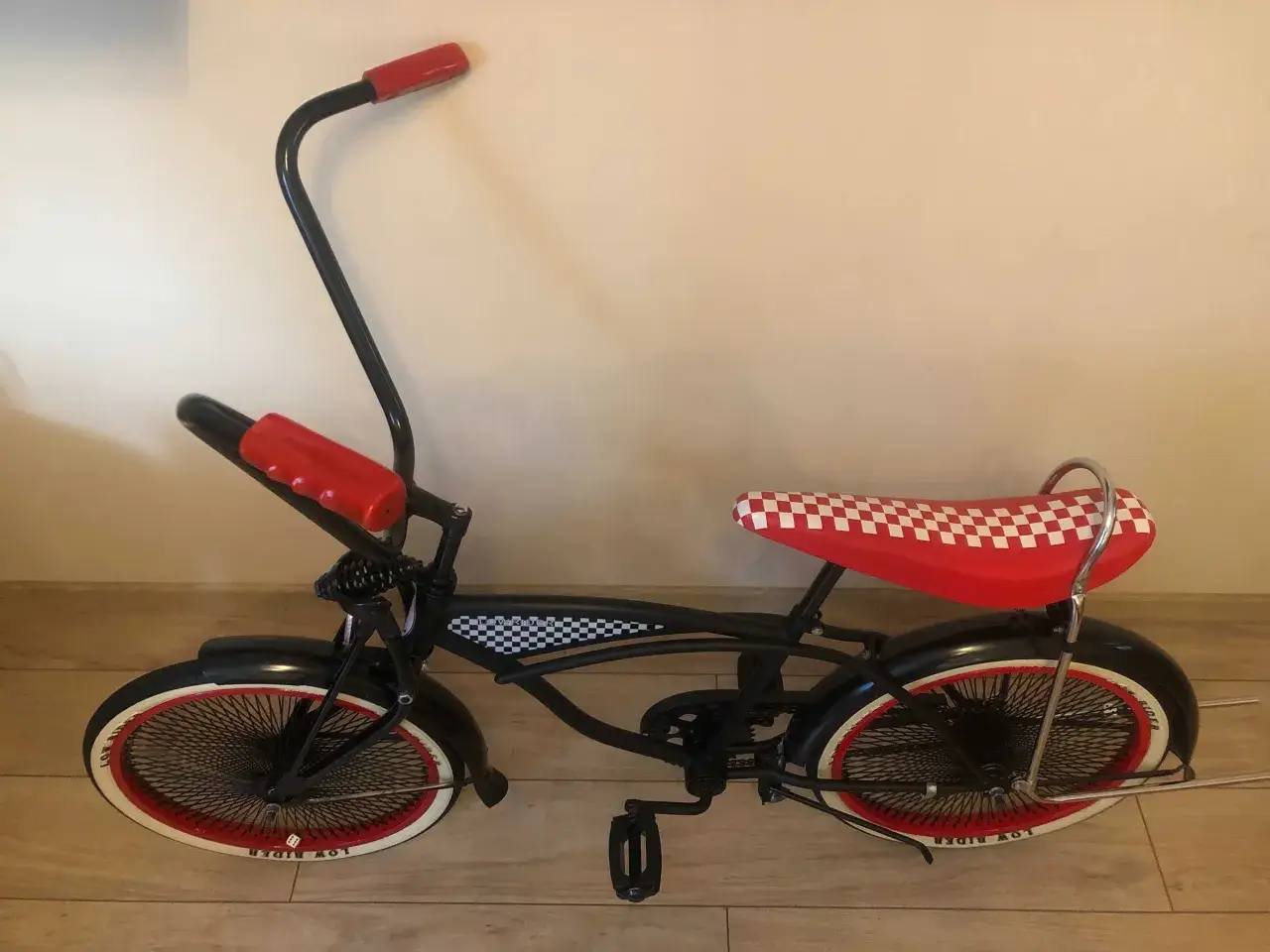 Czarny rower typu lowrider z czerwonymi akcentami i siedzeniem w kratkę. Idealny na przejażdżki w stylu amerykańskim.