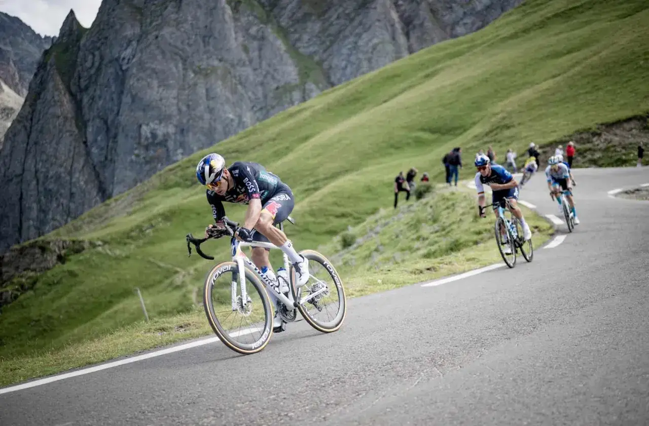 Kolarz na stromym podjeździe podczas Tour de France. Ile km jeszcze do mety? Widzowie dopingują na zboczu.