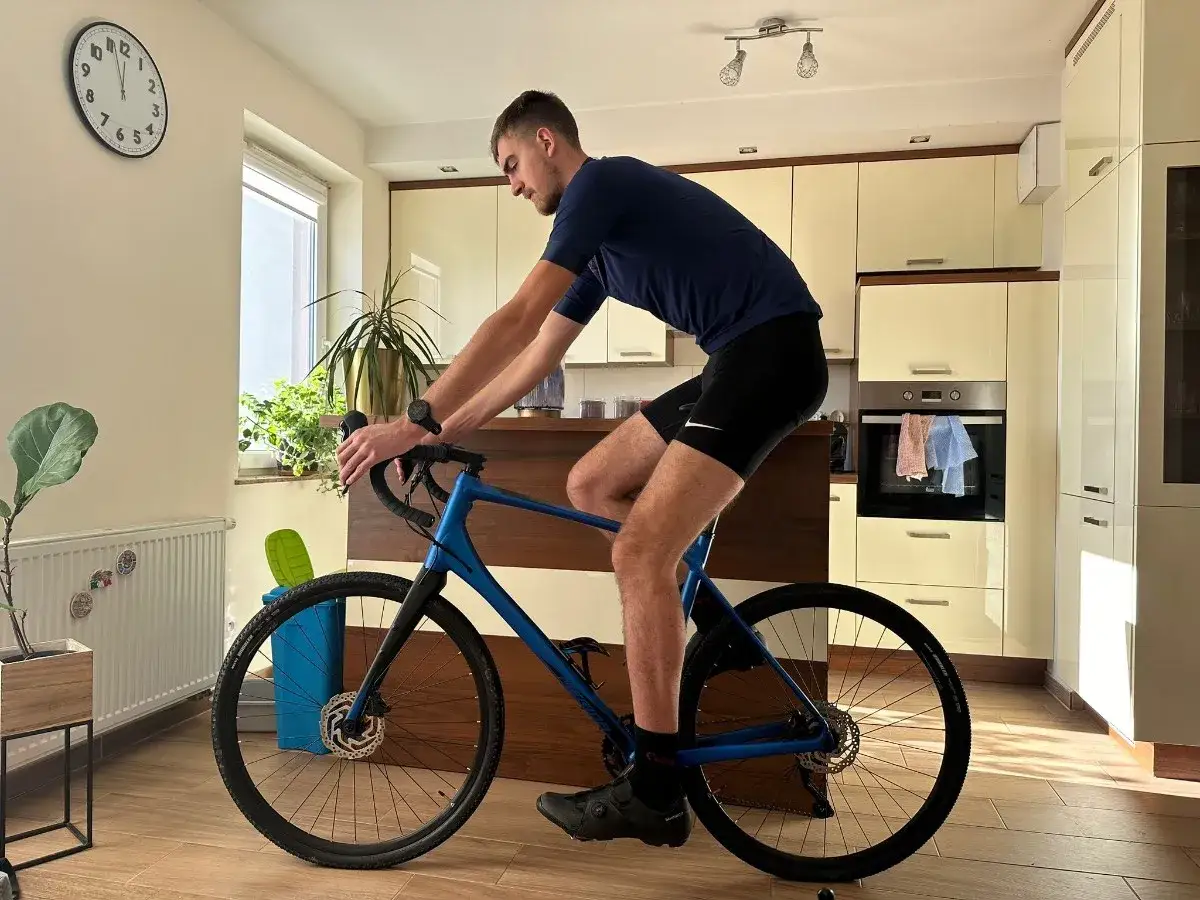 Mężczyzna w stroju kolarskim ćwiczy pozycję na rowerze gravel w domowym zaciszu.