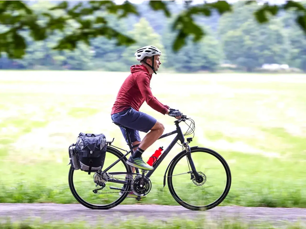 Mężczyzna w kasku jedzie na rowerze trekkingowym z sakwami, gotowy na wyprawę.