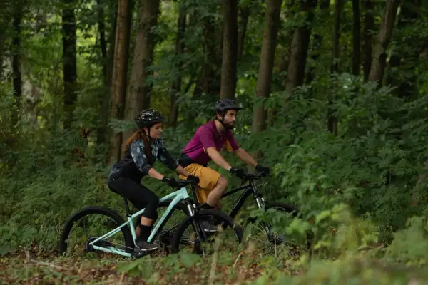 Para jadąca na rowerach górskich przez las. Czy to gravel, czy MTB? Trudno powiedzieć, ale zabawa jest przednia!