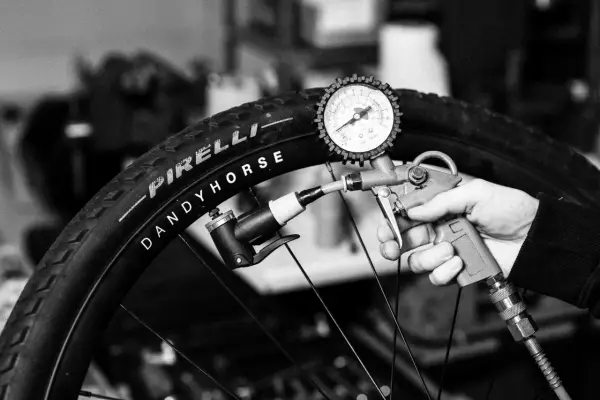 Ręka trzyma pompkę z manometrem, pompując oponę rowerową Pirelli Dandy Horse. Brak dętki.